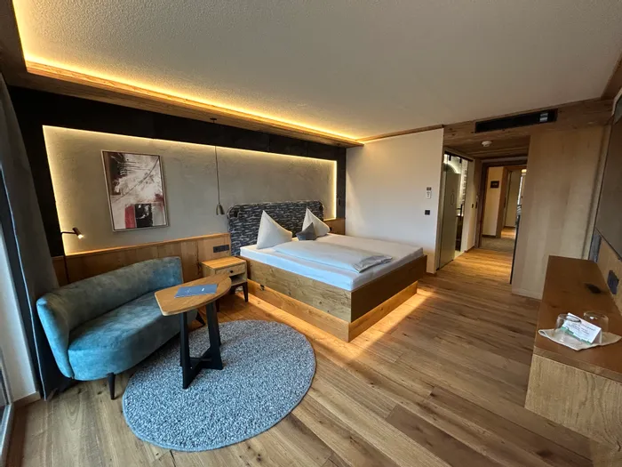 Camera d'hotel moderna con pavimento in legno, letto matrimoniale, divano e illuminazione soffusa